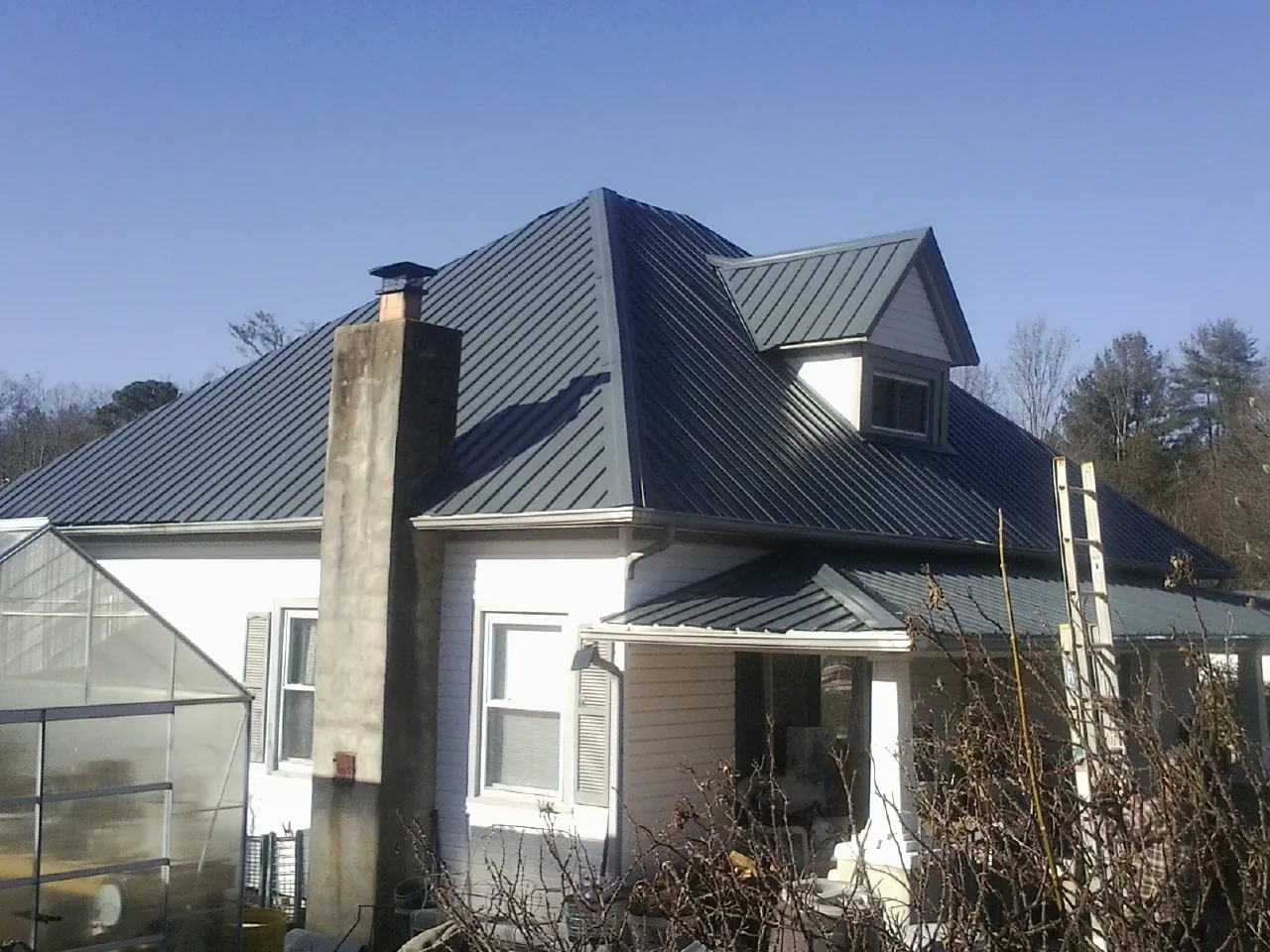 Dark blue standing seam metal roof on a white farmhouse with dormer — Slate & Tile Roof Repair by Roofing Brothers in Moncure