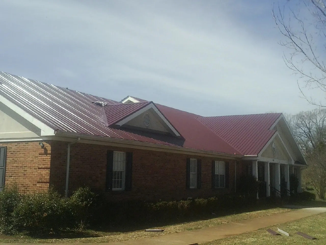 Red metal roof with gabled entries on a long brick building, from a Hail Damage Roof Repair job in Moncure