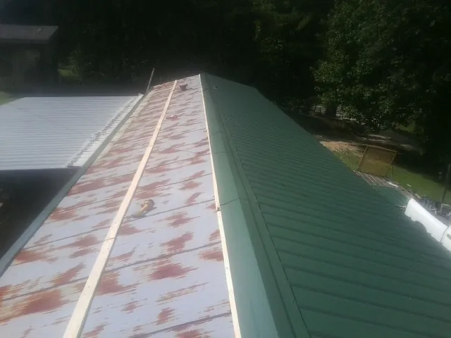 Old rusted panels beside newly installed green metal roofing — Wind Damage Roof Repair by Roofing Brothers in Moncure