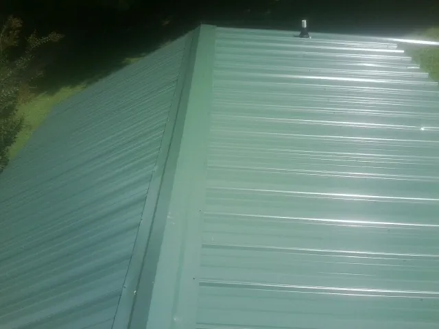 New green metal panels meeting at the ridge of a roof — Flat Roof Repair work by our crew in Moncure