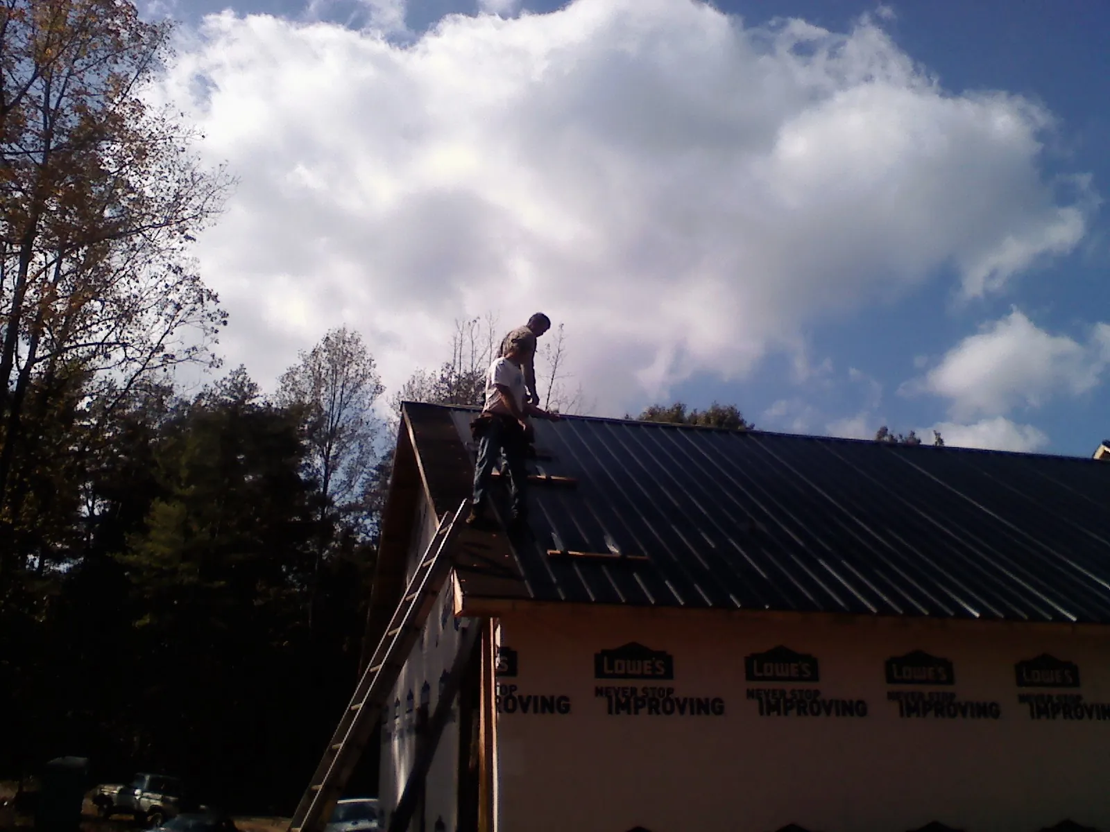 Roofer fastening dark metal panels high against a cloudy sky, from a Roof Inspection job in Moncure