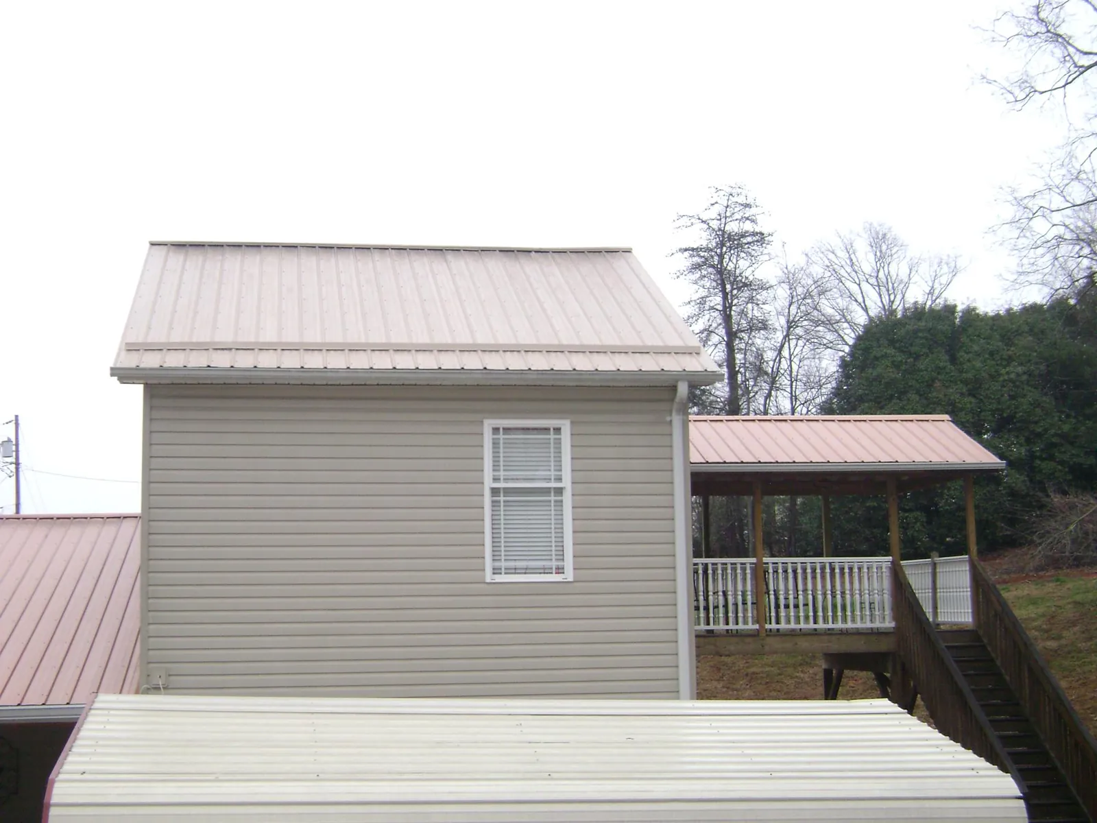 Tan metal roofs on a two story addition and attached porch, from a Roof Replacement job in Moncure